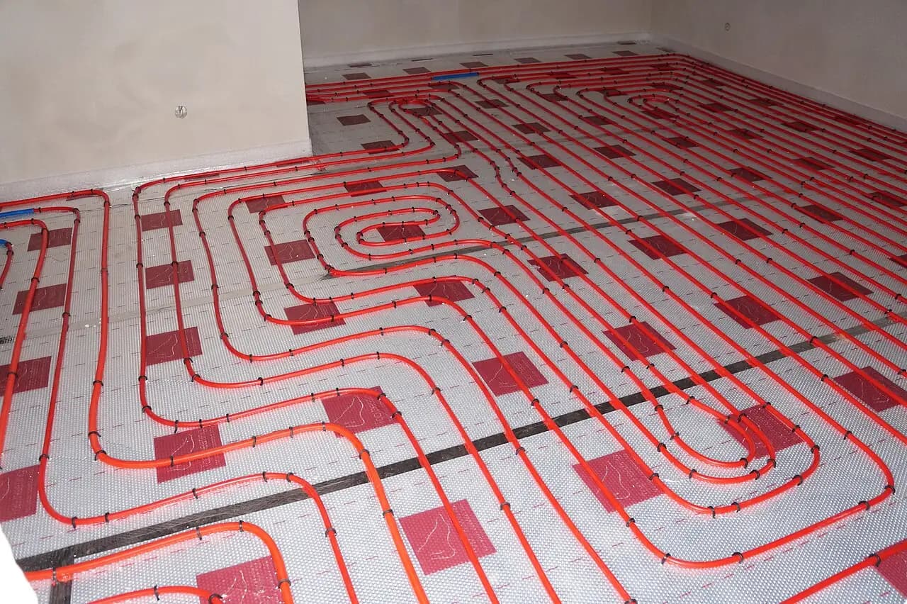 Red hot-water heating tubing laid in loops across a whole room's insulated floor, the hydronic kind of radiant floor