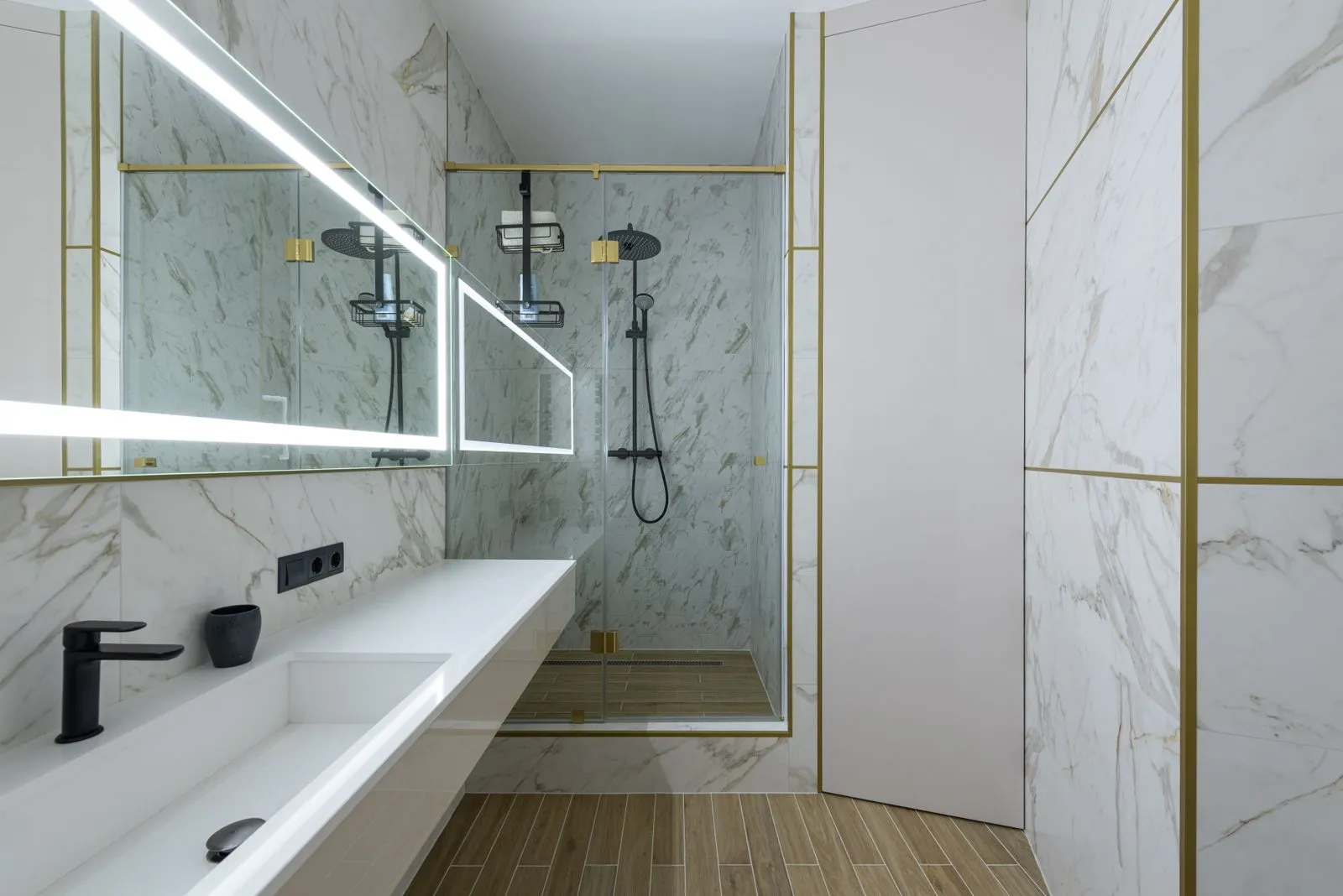 Bathroom with a wood-look porcelain tile floor, marble-look wall tile, a glass walk-in shower and a long white vanity under a lit mirror