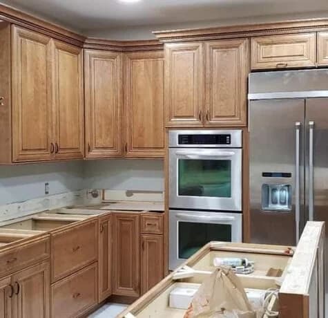 Stained wood raised-panel kitchen cabinets with a built-in double wall oven and stainless refrigerator during a Foreverbuilt installation in NJ